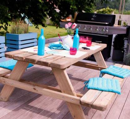 Mesa de conjunto de jardim para piquenique com almofadas decorativas, junto a barbecue com petisco para picnic